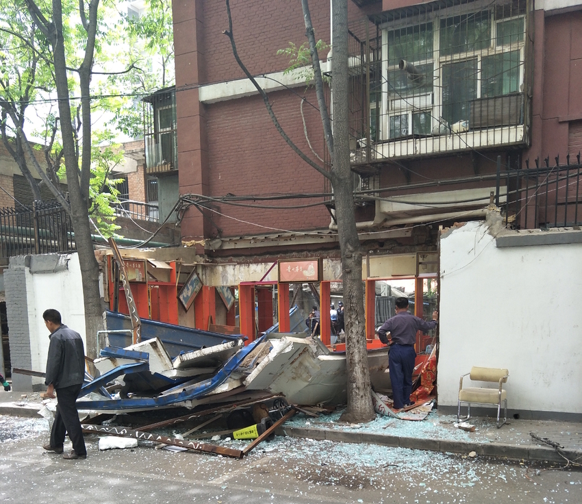 a man surveys the damage of a demolished liquor store on a Beijing back street